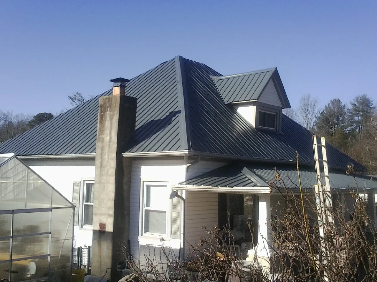 Dark blue standing seam metal roof on a white farmhouse with dormer — Slate & Tile Roof Repair by Roofing Brothers in Onaga