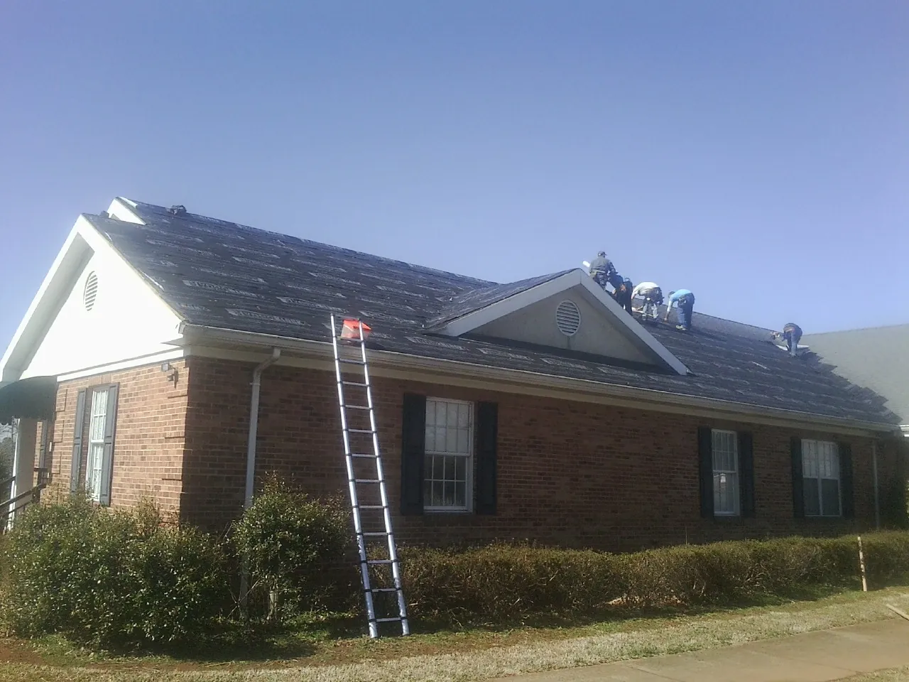 Crew tearing shingles off a brick ranch roof with a ladder set — Emergency Roof Repair work by our crew in Onaga
