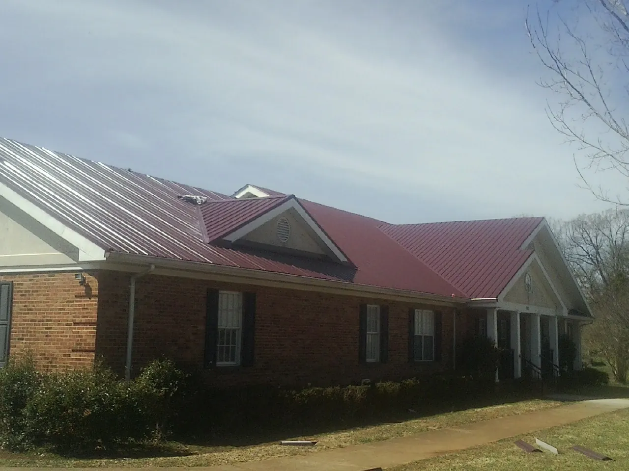 Red metal roof with gabled entries on a long brick building, from a Hail Damage Roof Repair job in Onaga