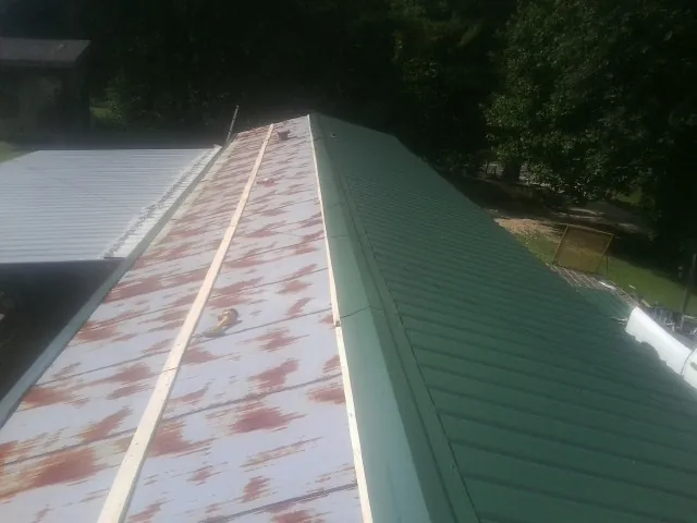 Old rusted panels beside newly installed green metal roofing — Wind Damage Roof Repair by Roofing Brothers in Onaga