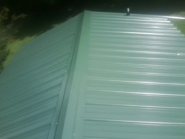 New green metal panels meeting at the ridge of a roof — Flat Roof Repair work by our crew in Onaga