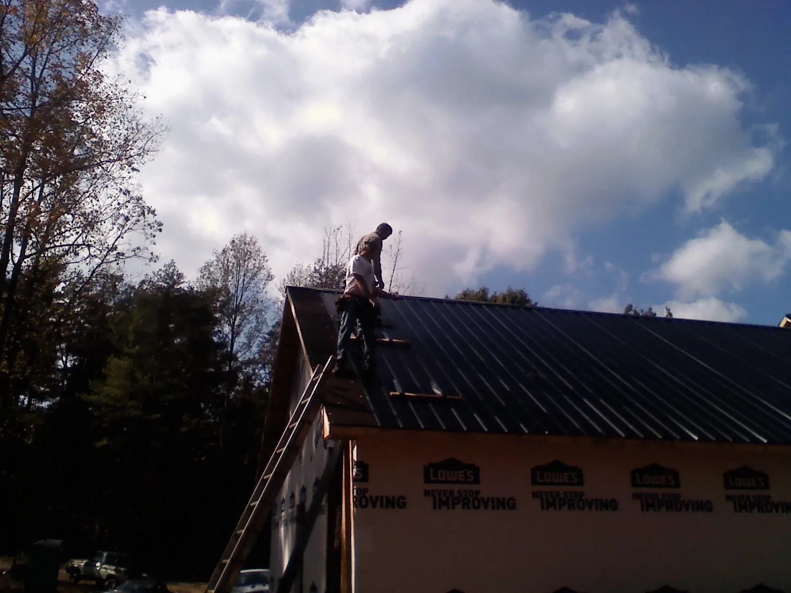 Roofer fastening dark metal panels high against a cloudy sky, from a Roof Inspection job in Onaga