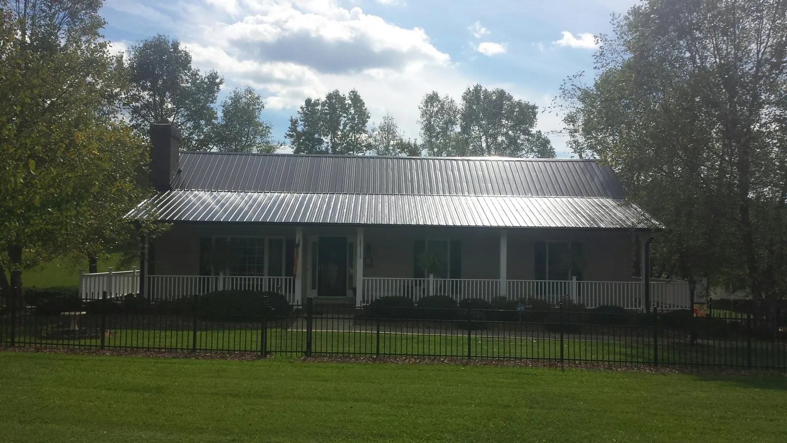 Gray metal roof on a brick ranch with a full width front porch — Gutter Guard Installation work by our crew in Onaga