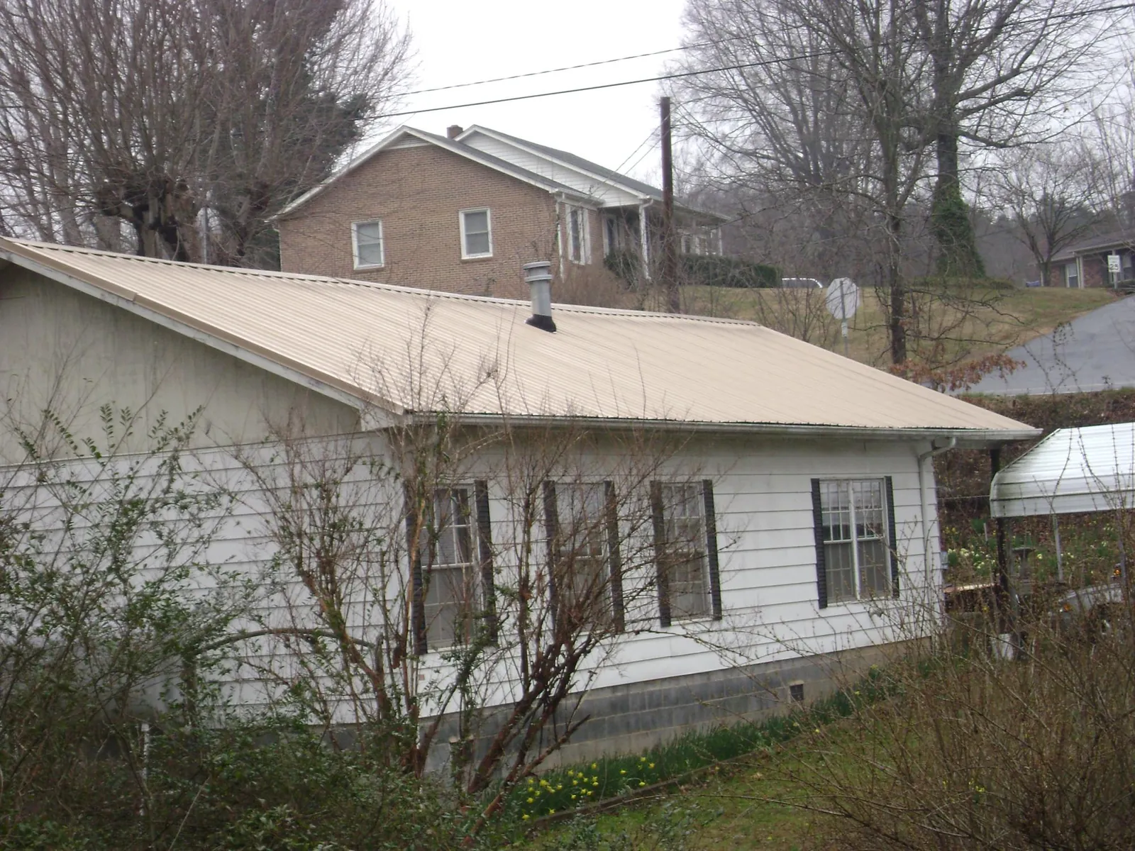 Tan metal roof on a white sided house set into a hillside — Commercial Roofing by Roofing Brothers in Onaga
