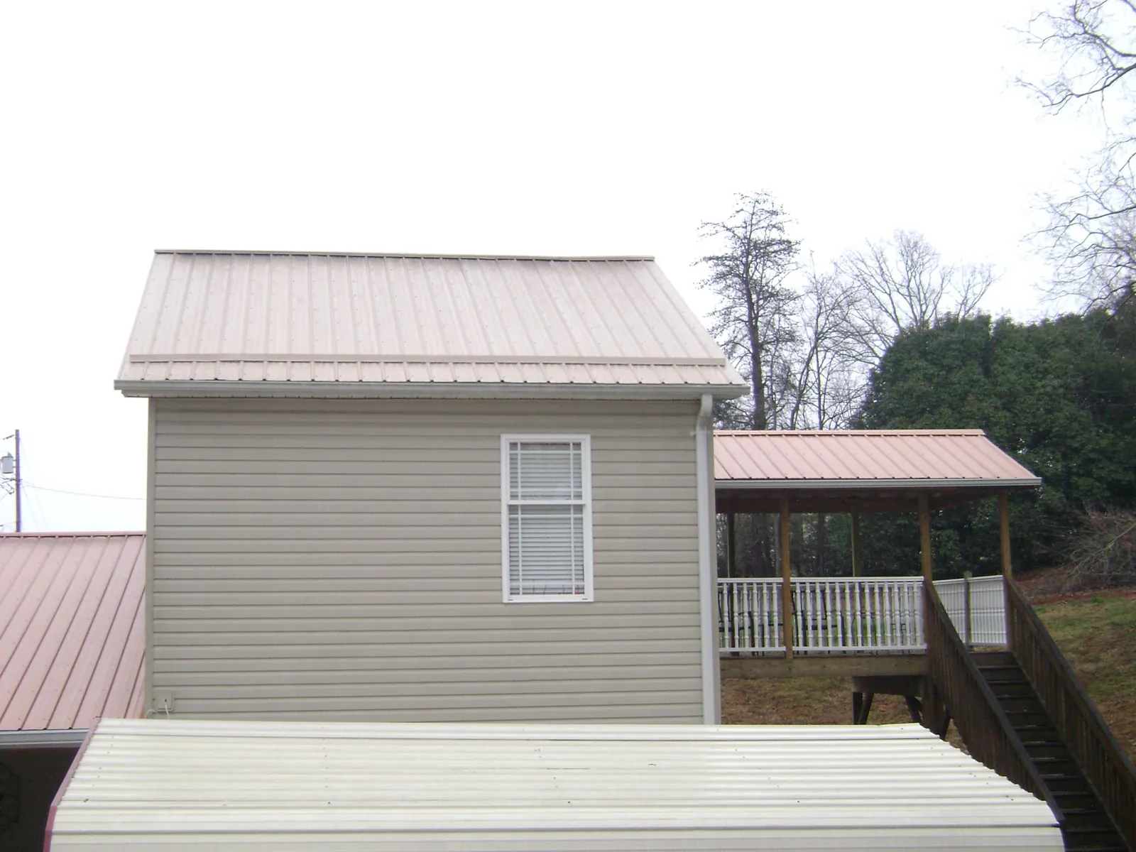 Tan metal roofs on a two story addition and attached porch, from a Roof Replacement job in Onaga
